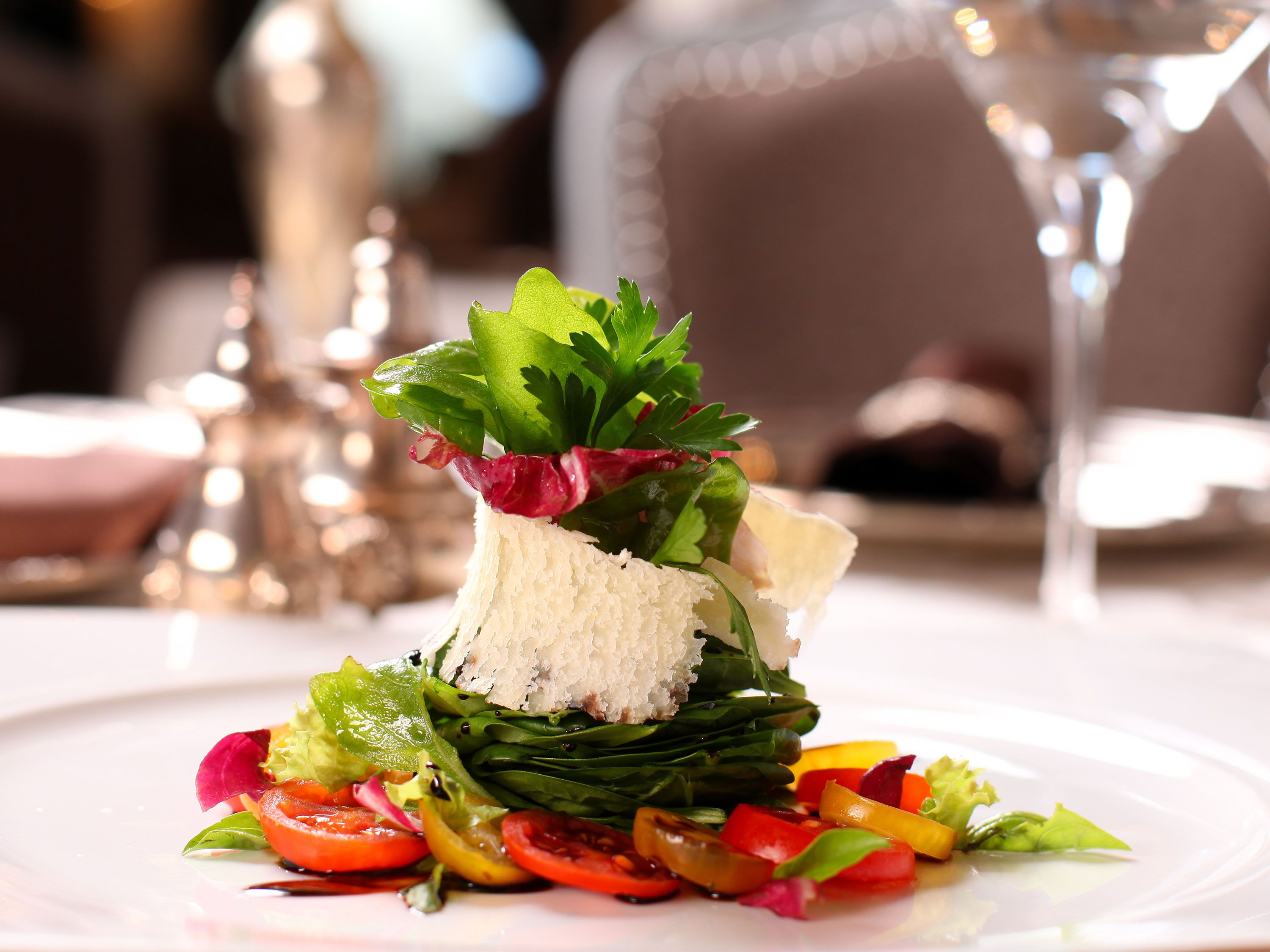 Gourmet layered salad topped with shaved cheese, fresh herbs, and colorful vegetables.