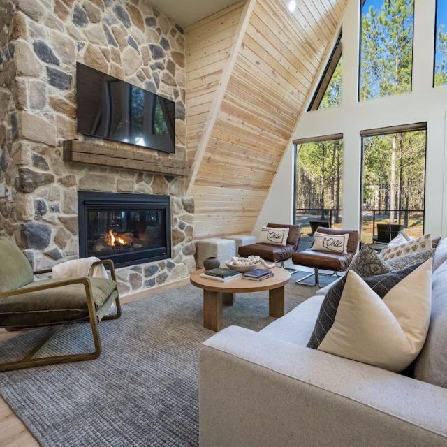 A living room of an A-frame cabin Vrbo, with large fire and TV, in Broken Bow