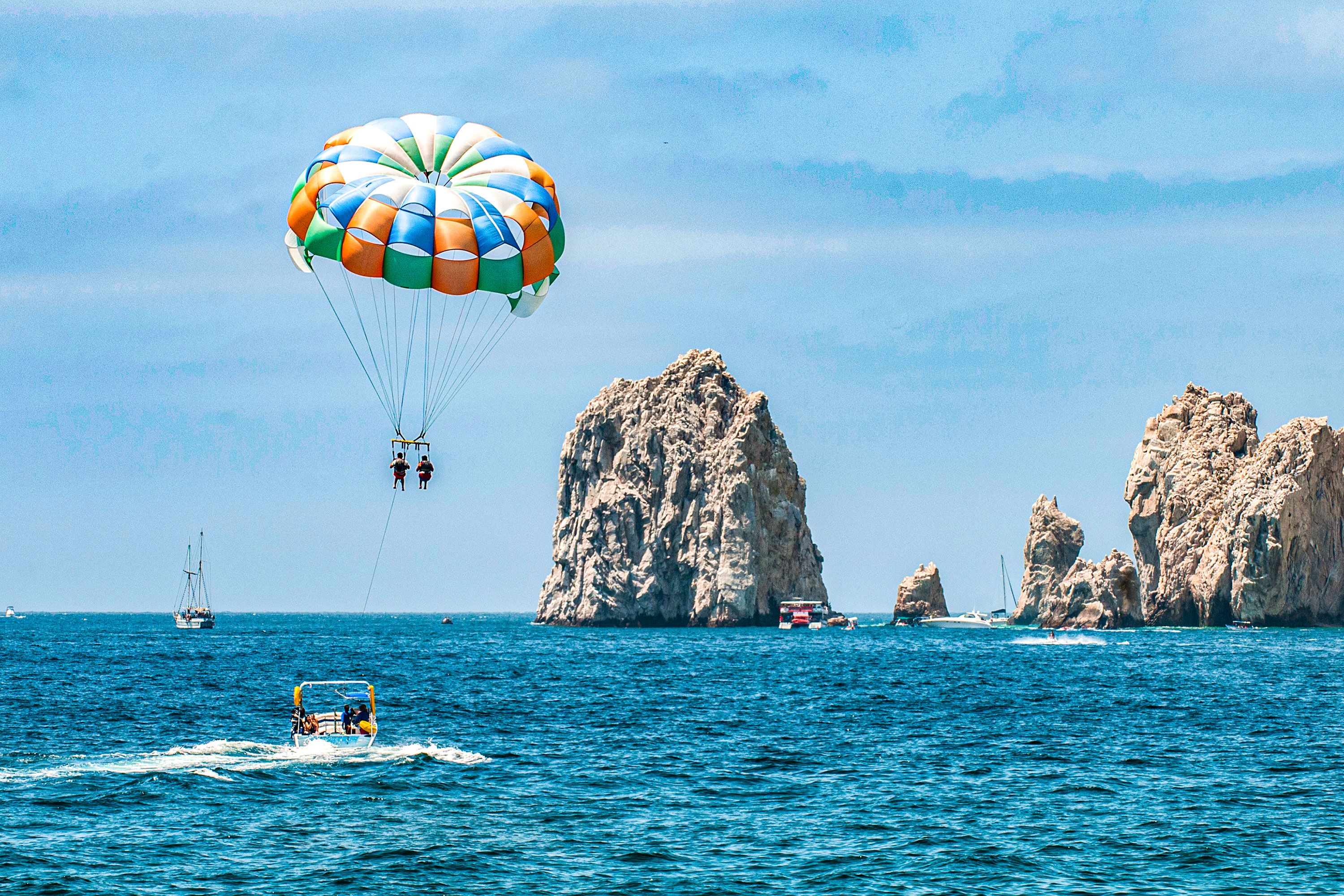 Two people parasailing above the ocean near Cabo’s iconic rock formations.