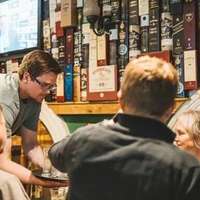 A man sets a tray of drinks down for four drinkers at the table in a traditional Dublin pub