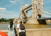 Two people seen from behind lean on the wall and look out over the River Thames to Tower Bridge on a sunny day in London, England, UK