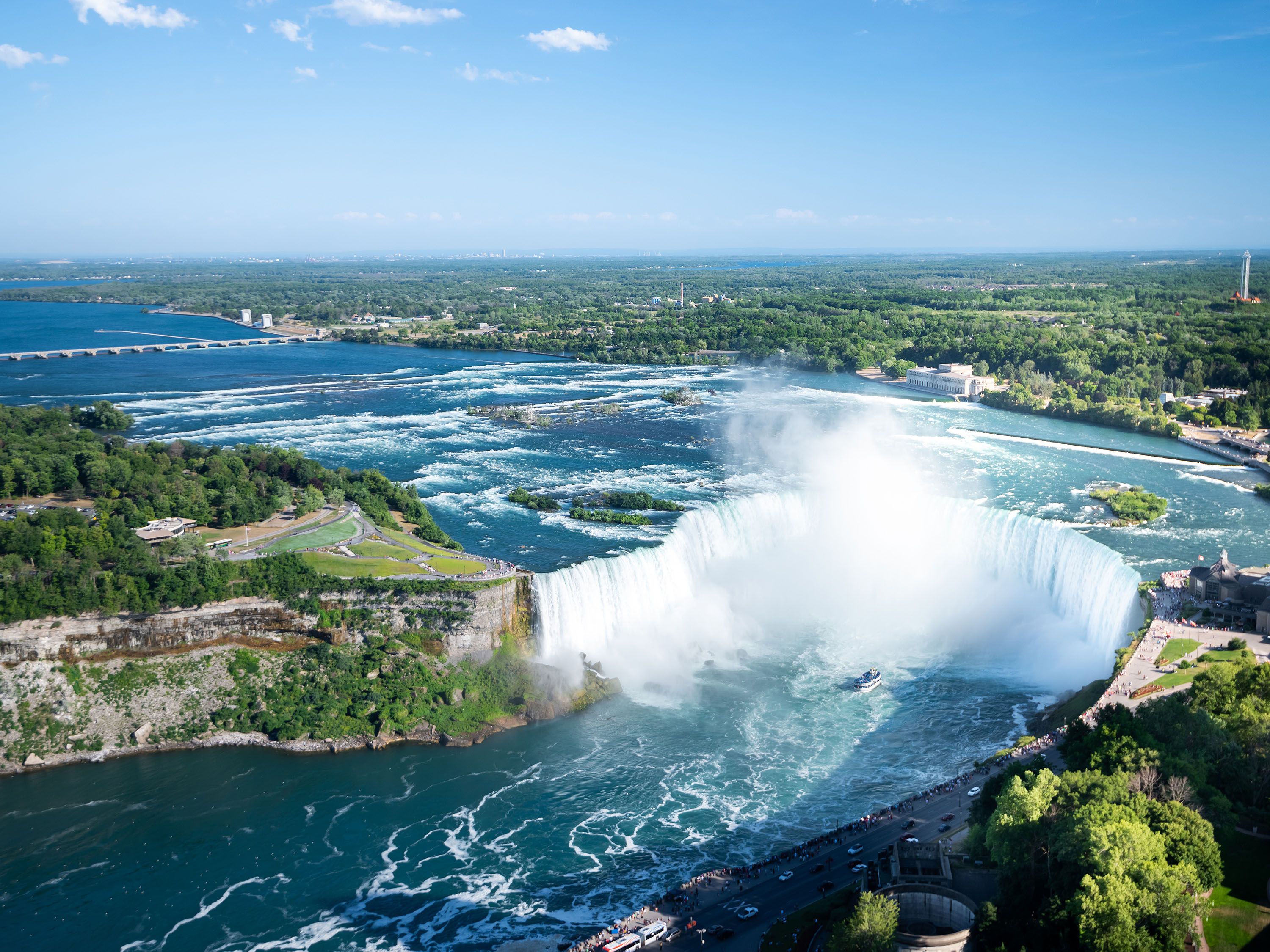 Overhead view of Niagara Falls with cliffs on either side and town in distance.