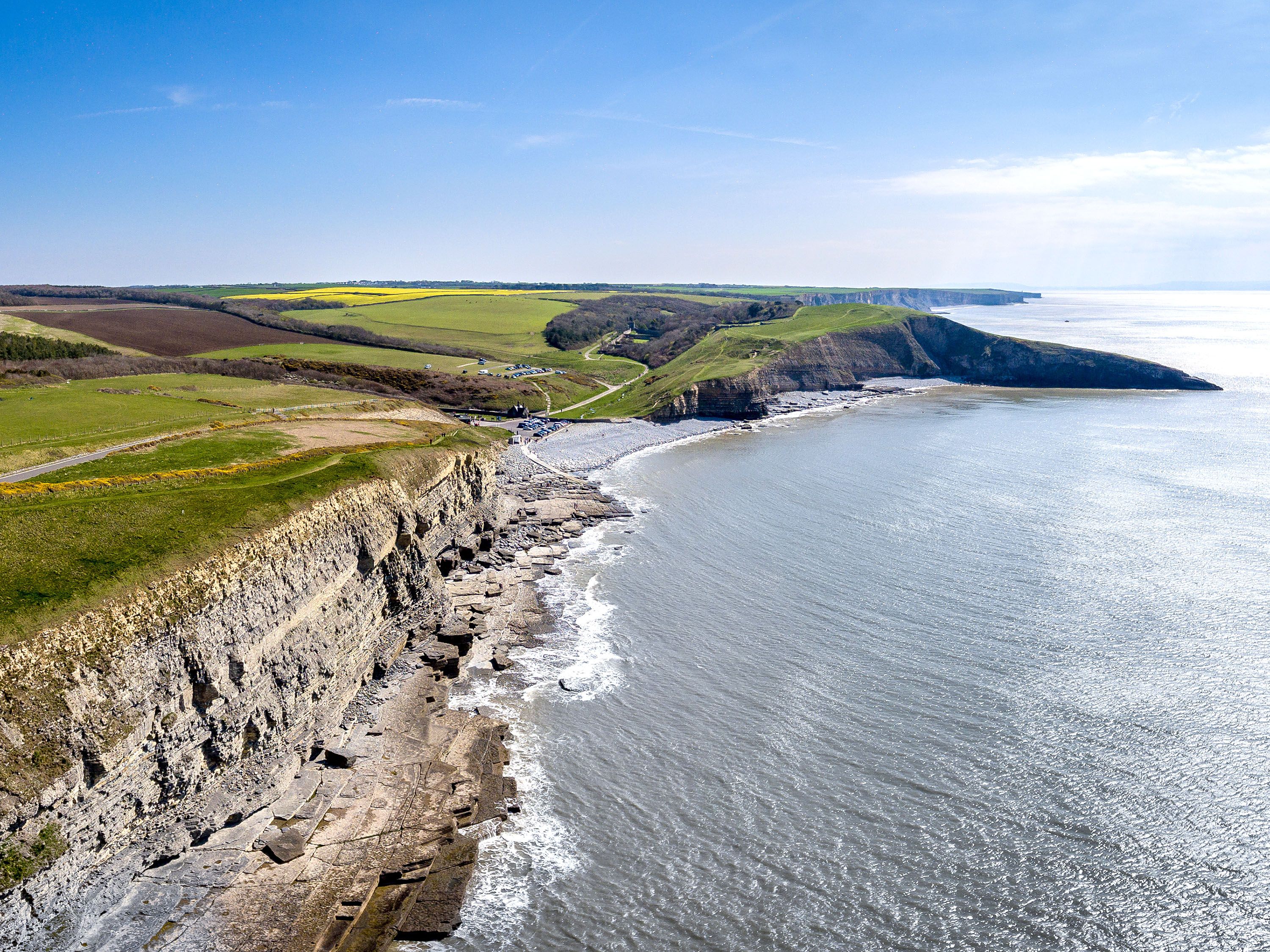Aerial view of lush green grass and a cliff overlookng the ocean.