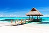 A wooden beachfront gazebo on a white sandy beach with clear blue tropical ocean in the background.