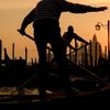 Gondoliers in classic striped shirts paddle their oars in the canal at sunset in Venice, Italy