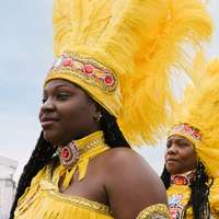 Two women wearing elaborate costumes including headdresses decorated with yellow feathers, red and yellow jewels and gold embroidery, at the New Orleans Jazz & Heritage Festival