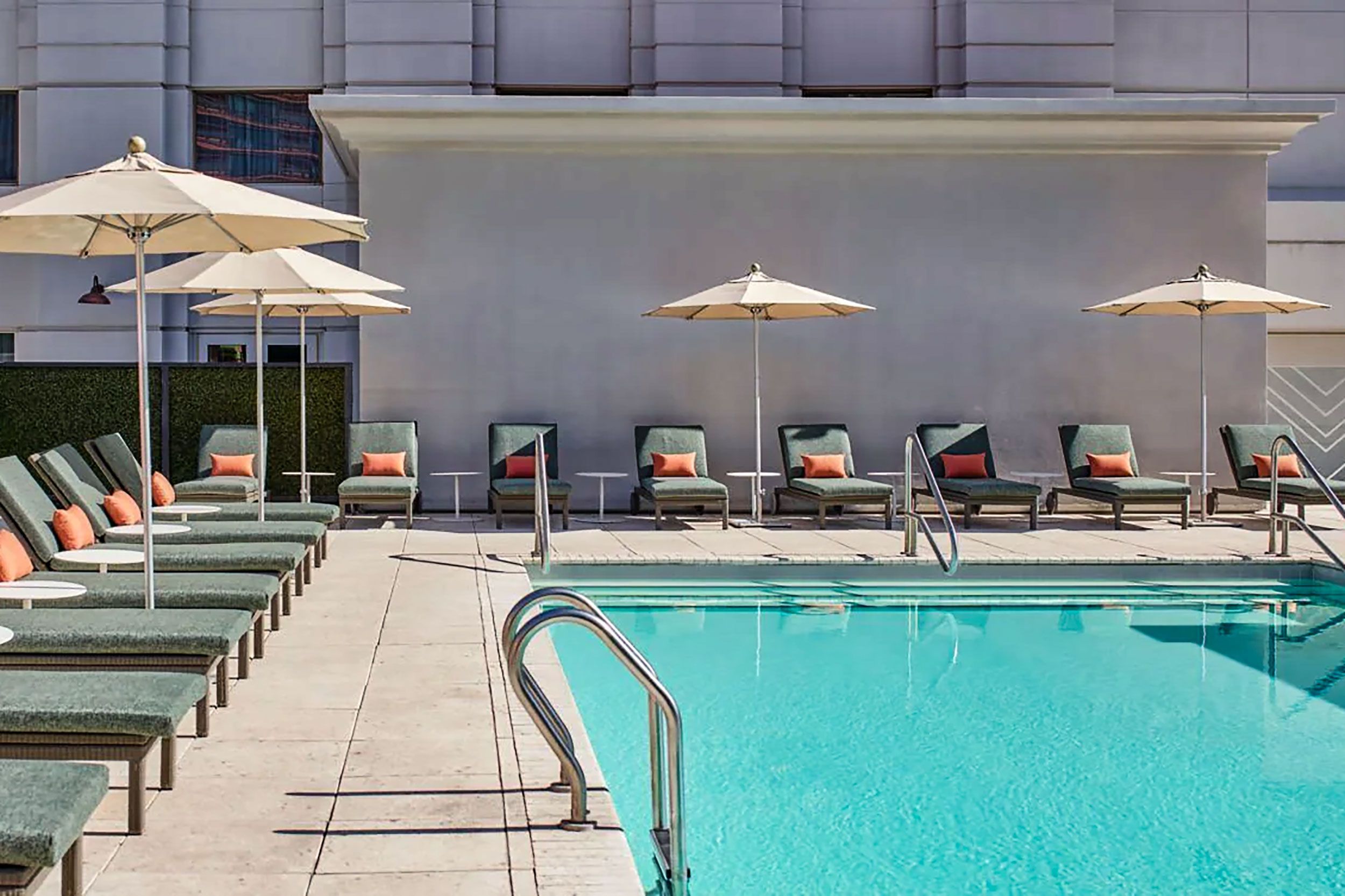 A rectangular pool is surrounded by lounge chairs and parasols in the sun.