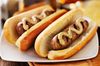 Two bratwursts in buns covered with mustard sitting on a white plate.