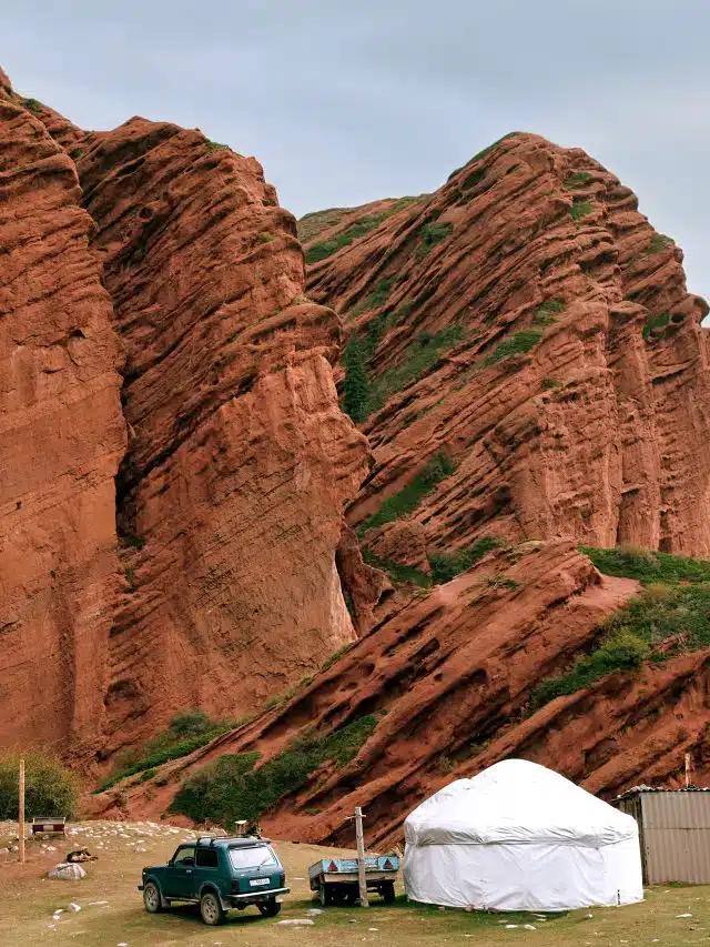The dramatic diagonal structures of the red-rock Jety-Oguz canyon, Kyrgyzstan, with a jeep and white yurt