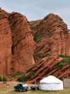 The dramatic diagonal structures of the red-rock Jety-Oguz canyon, Kyrgyzstan, with a jeep and white yurt