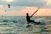A person leans back as they kitesurf on the sea at sunset
