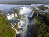 An aerial view of a sprawling stretch of water falling into a pool crevice, surrounded by green bushes on bordering rocks