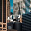 A white flying taxi helicopter passes in front of a skyline of office buildings in New York