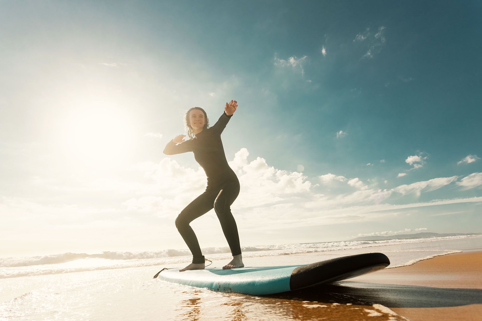 A woman standing on a surfboard on the beach during a surf lesson.