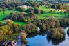 An aerial view of a large green park with a lake, winding paths, trees, and a stately building.
