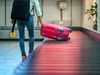 A man lifts a pink suitcase off of a baggage carousel at an airport.