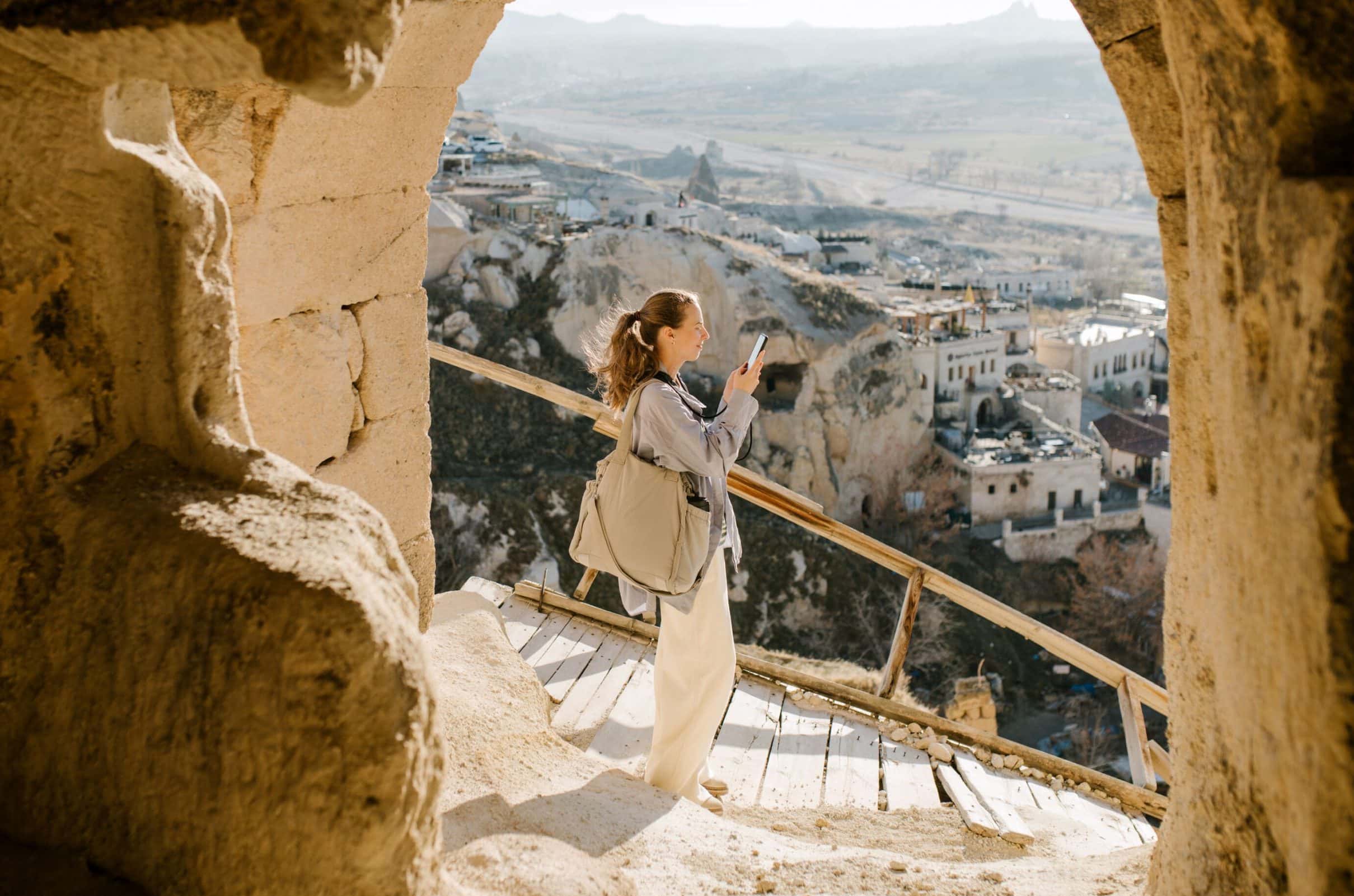 A woman pauses to take a picture on a wood-plank slope, a view of villages, a valley and mountains beyond