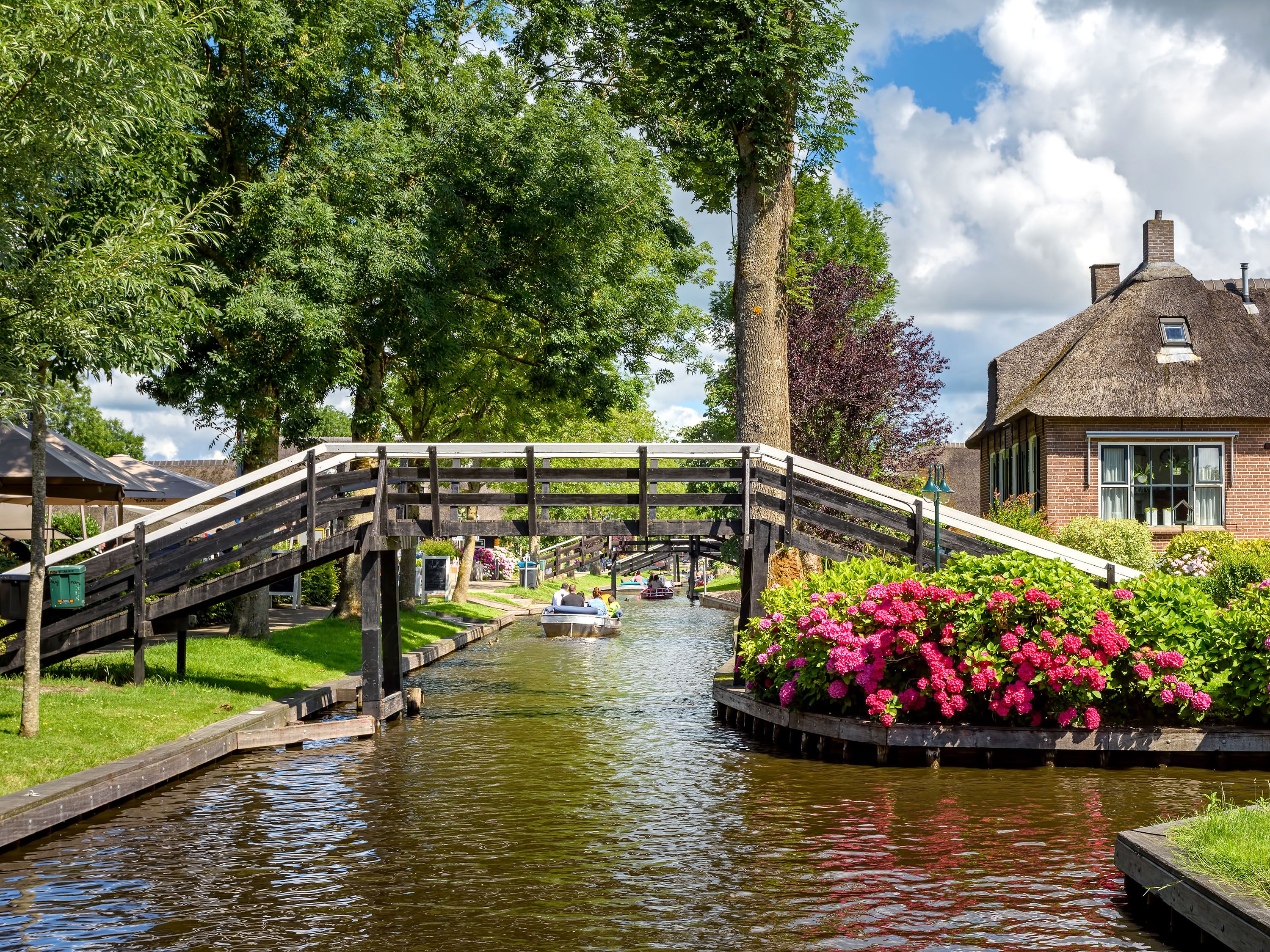 Bridge over canal lined with pink and red flowers.