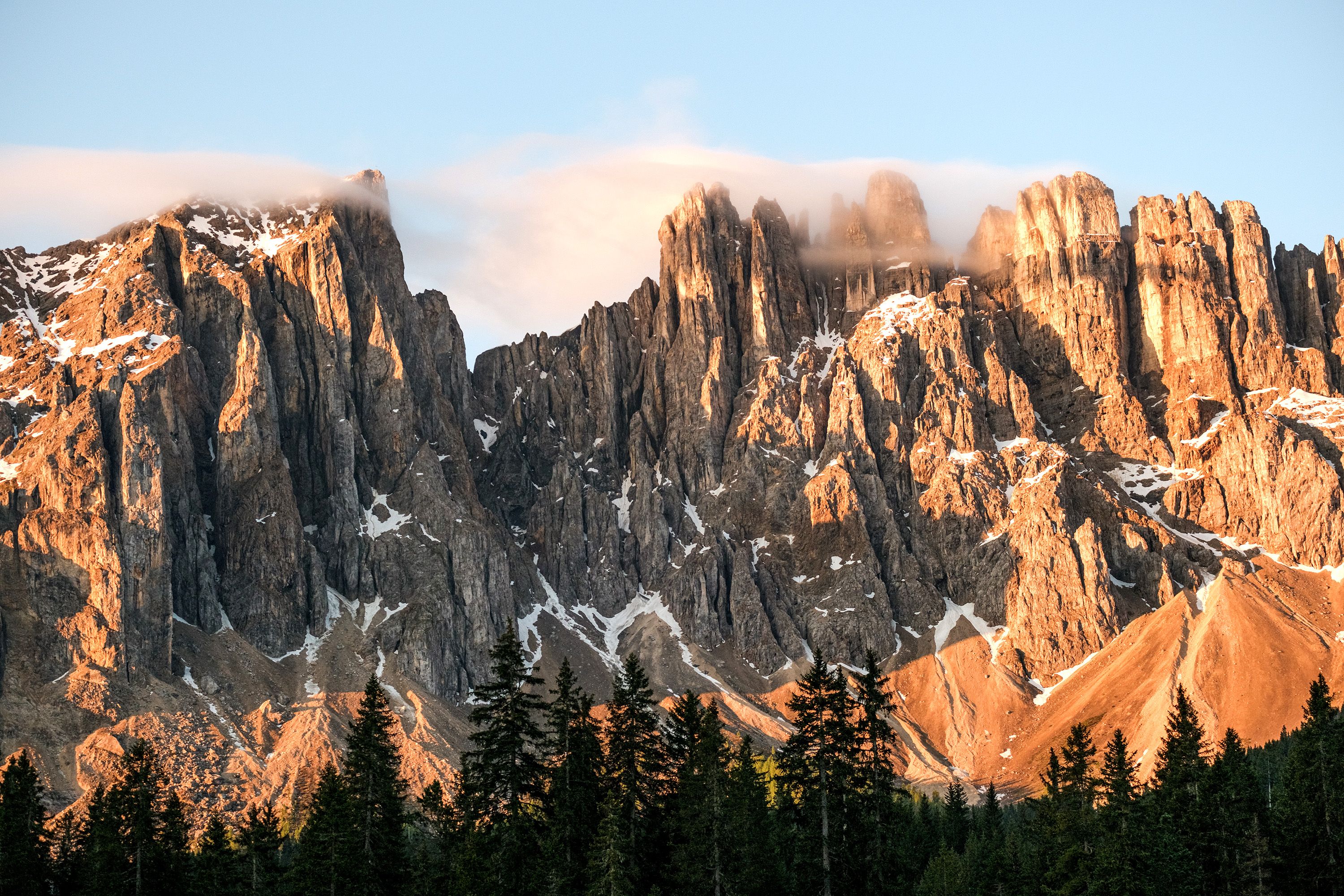 Italian dolomite mountain peaks with scattered snow reach into the clouds.
