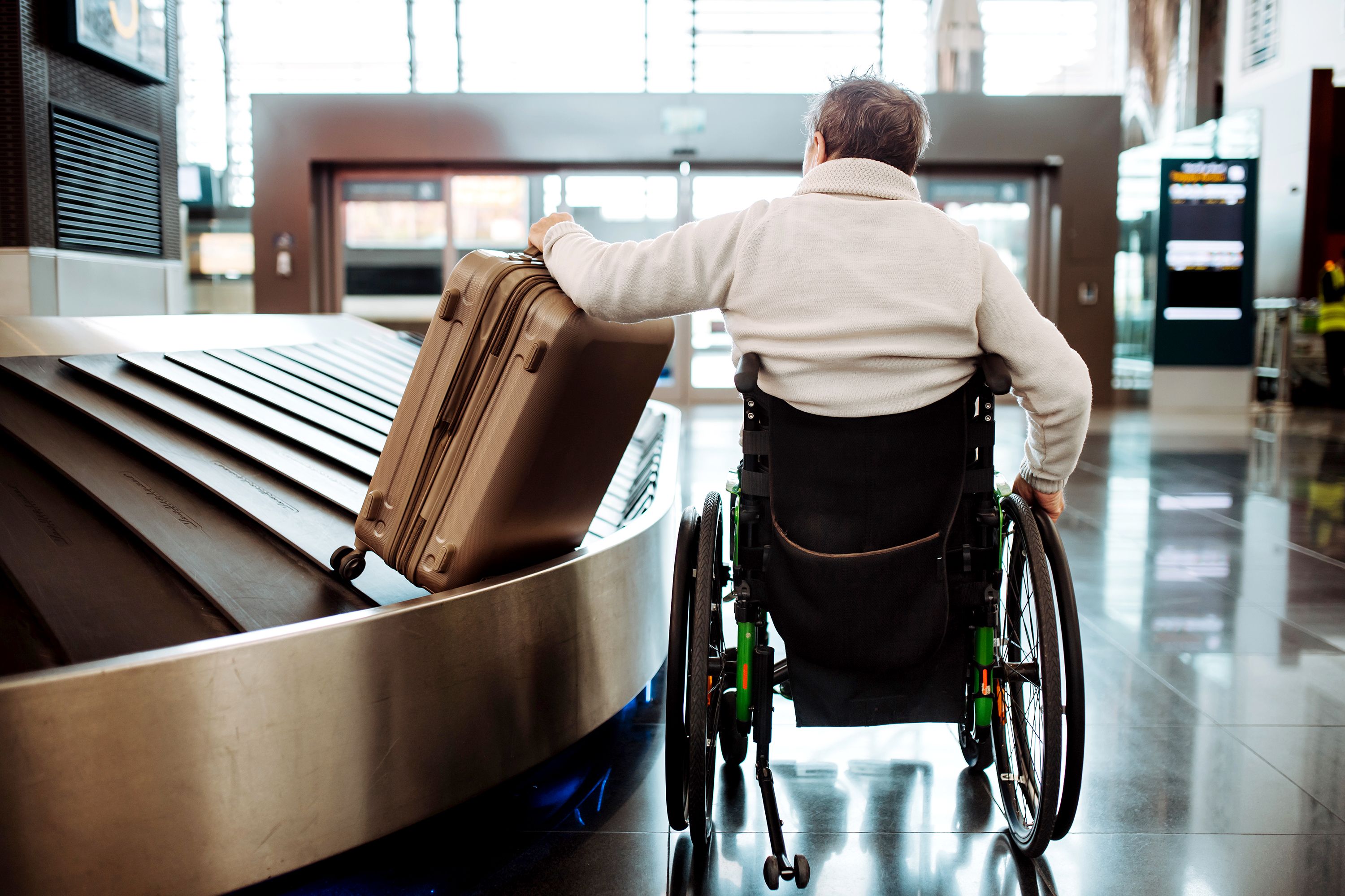 Person in a wheelchair retrieves their luggage from a carrousel.