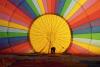 A person stands inside the envelope of a rainbow-colored hot-air balloon as it inflates