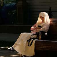 A woman in a headscarf, sitting on a bench in a shaft of sunlight, checks her phone. Shymkent, southern Kazakhstan