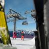 People ski beneath a chairlift on a clear day with blue skies in the French Alps