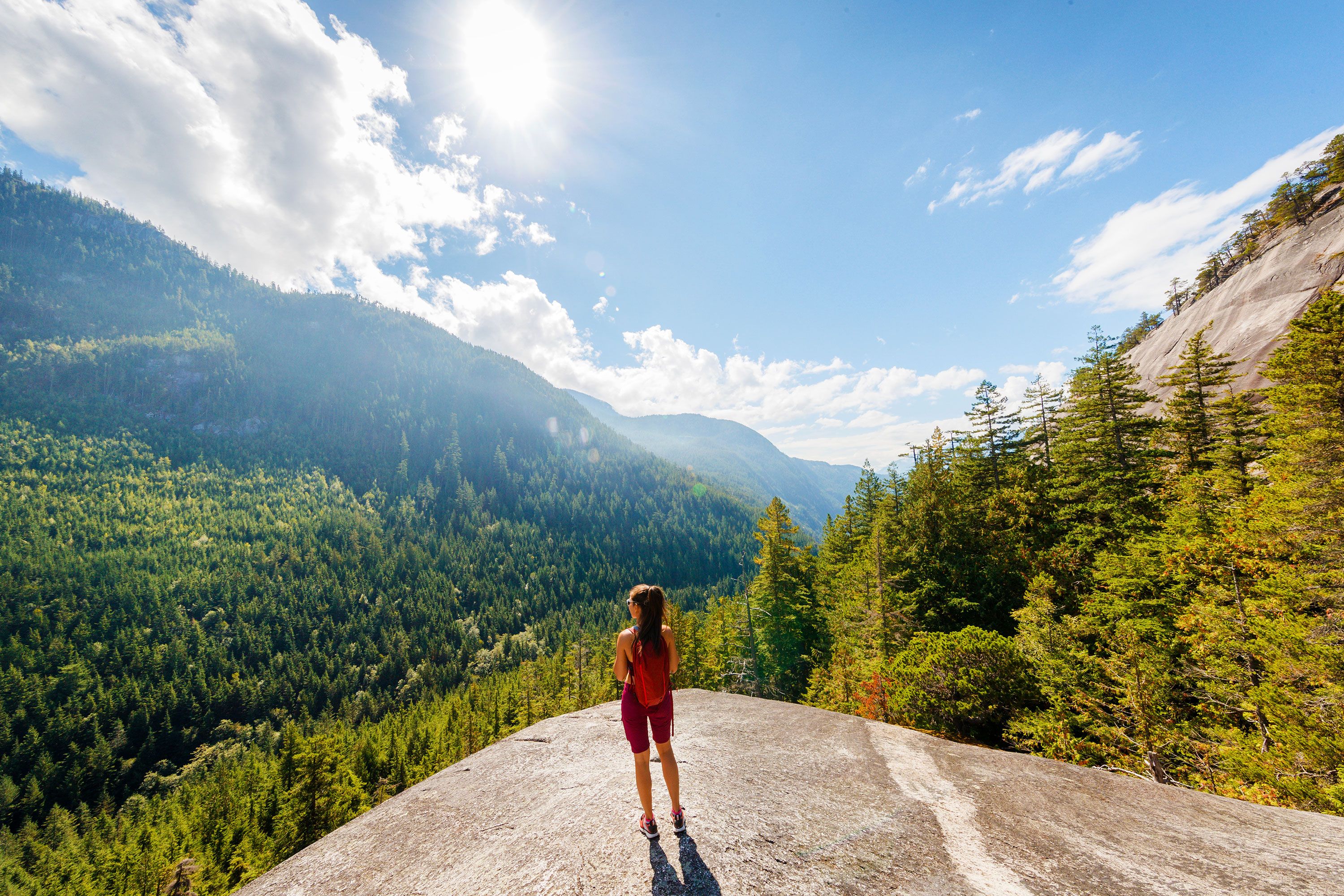 A woman hiker at the viewpoint on Squamish Stawamus Chief Mountain in British Columbia looking out over the trees.