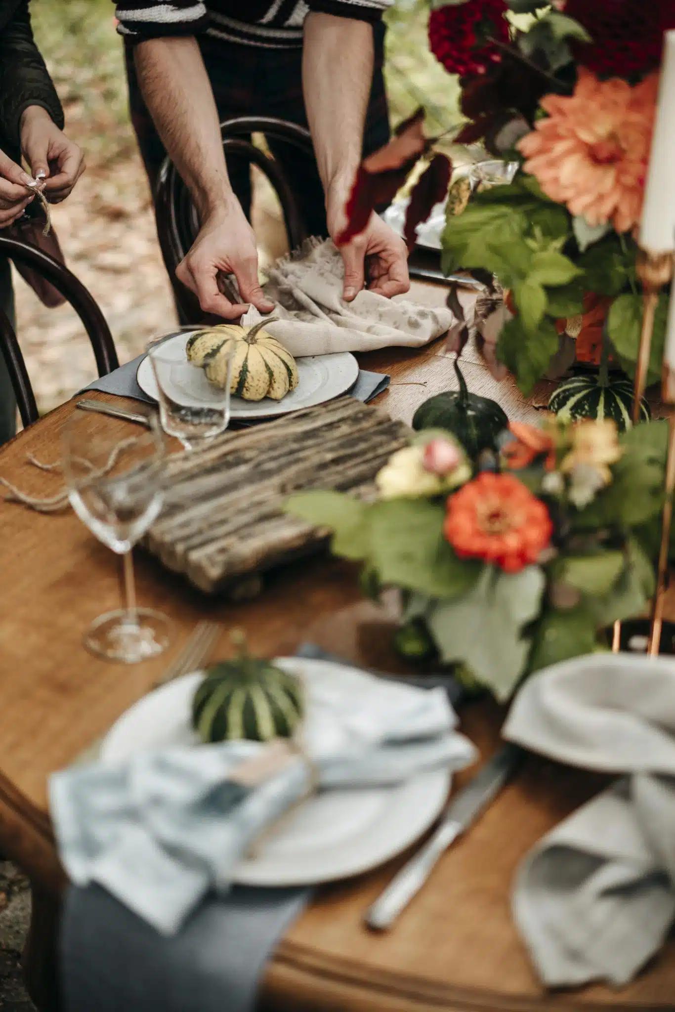 A rustic wooden table set with linen napkins, miniature pumpkins, and potted plants