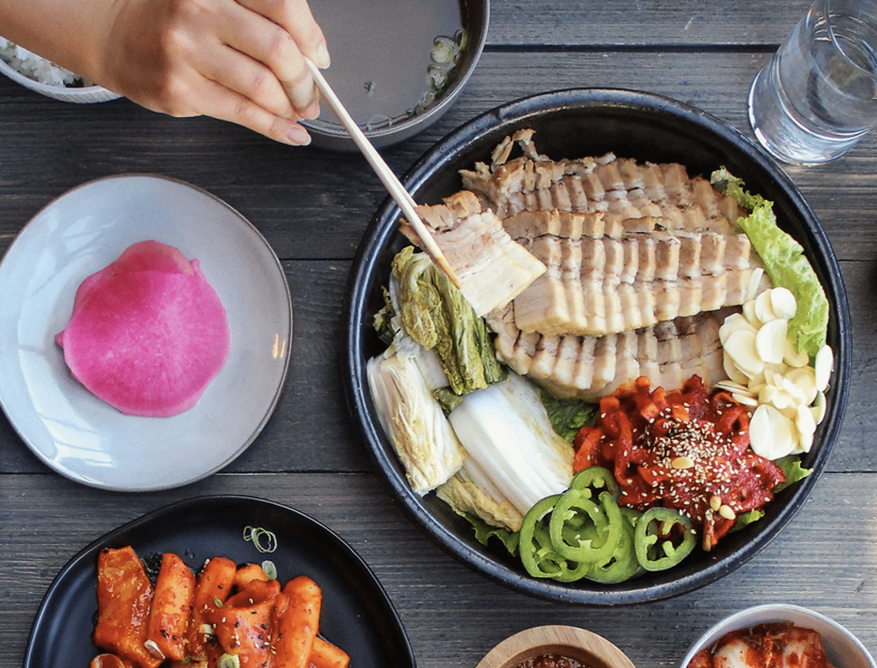 A person holding chopsticks picks a slice of tofu from a large bowl of brightly colored vegetarian food at Hangari in Koreatown, Los Angeles