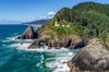 A lighthouse on a green rocky cliffside in an ocean cove.