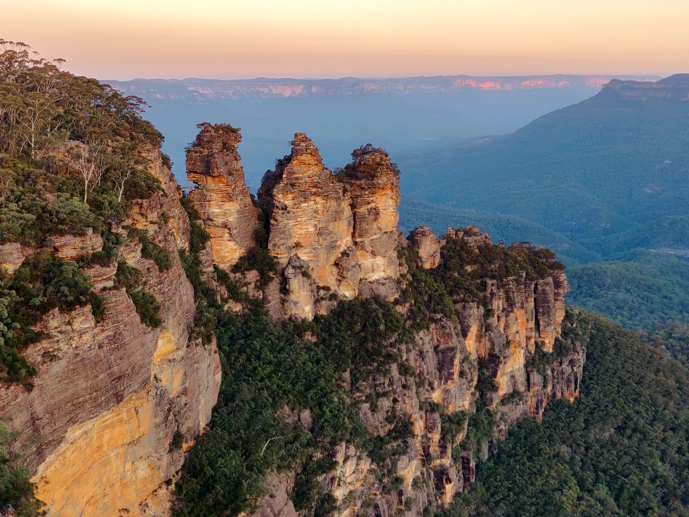 An aerial shot of the Three Sisters rock formation in the Blue Mountains National Park at sunset