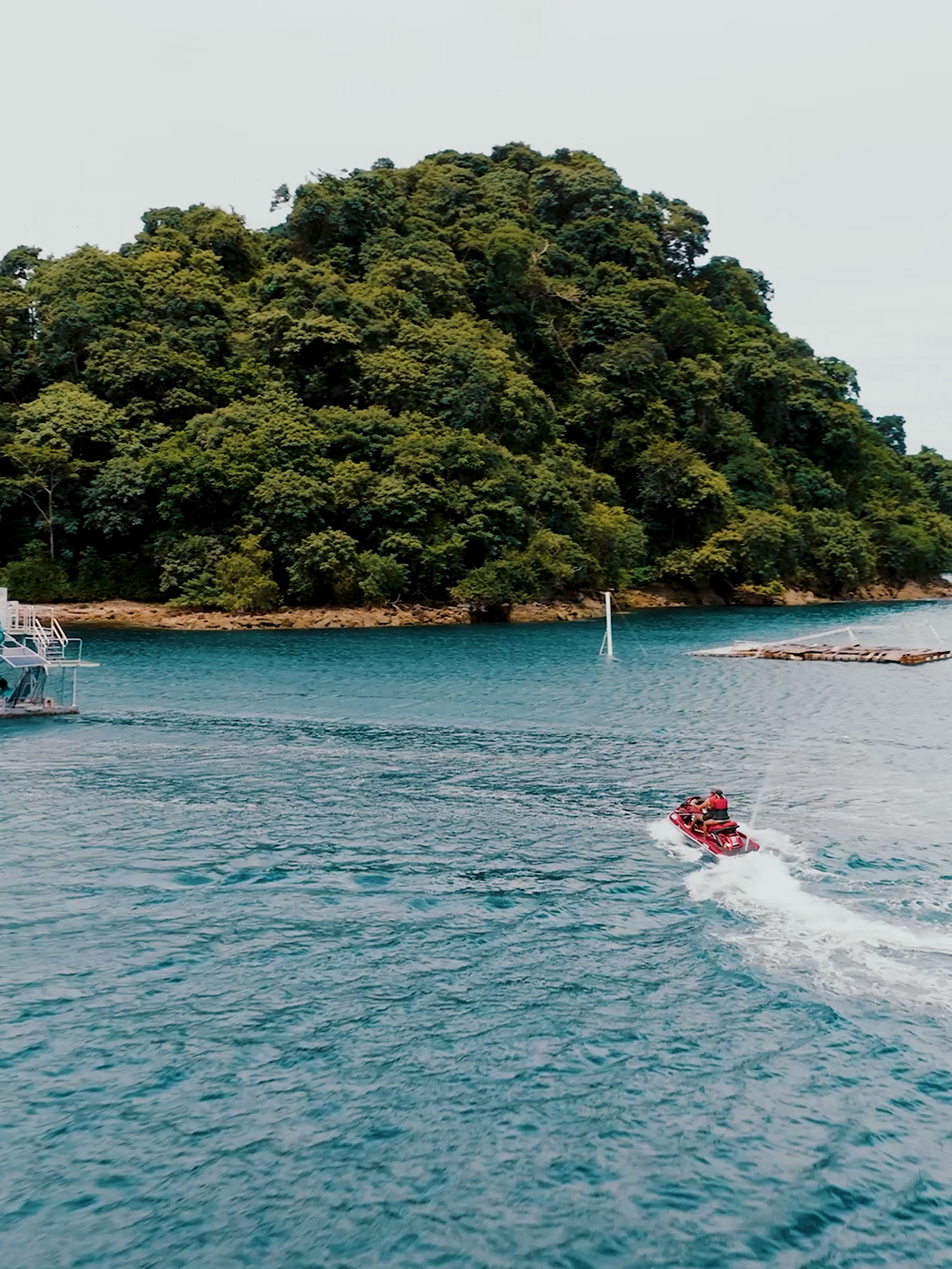 A boat drives through the blue sea towards an island with golden sand and green trees