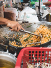 A person uses a metal utensil to stir traditional pad thai in a large wok at a street food stall in Bangkok, Thailand