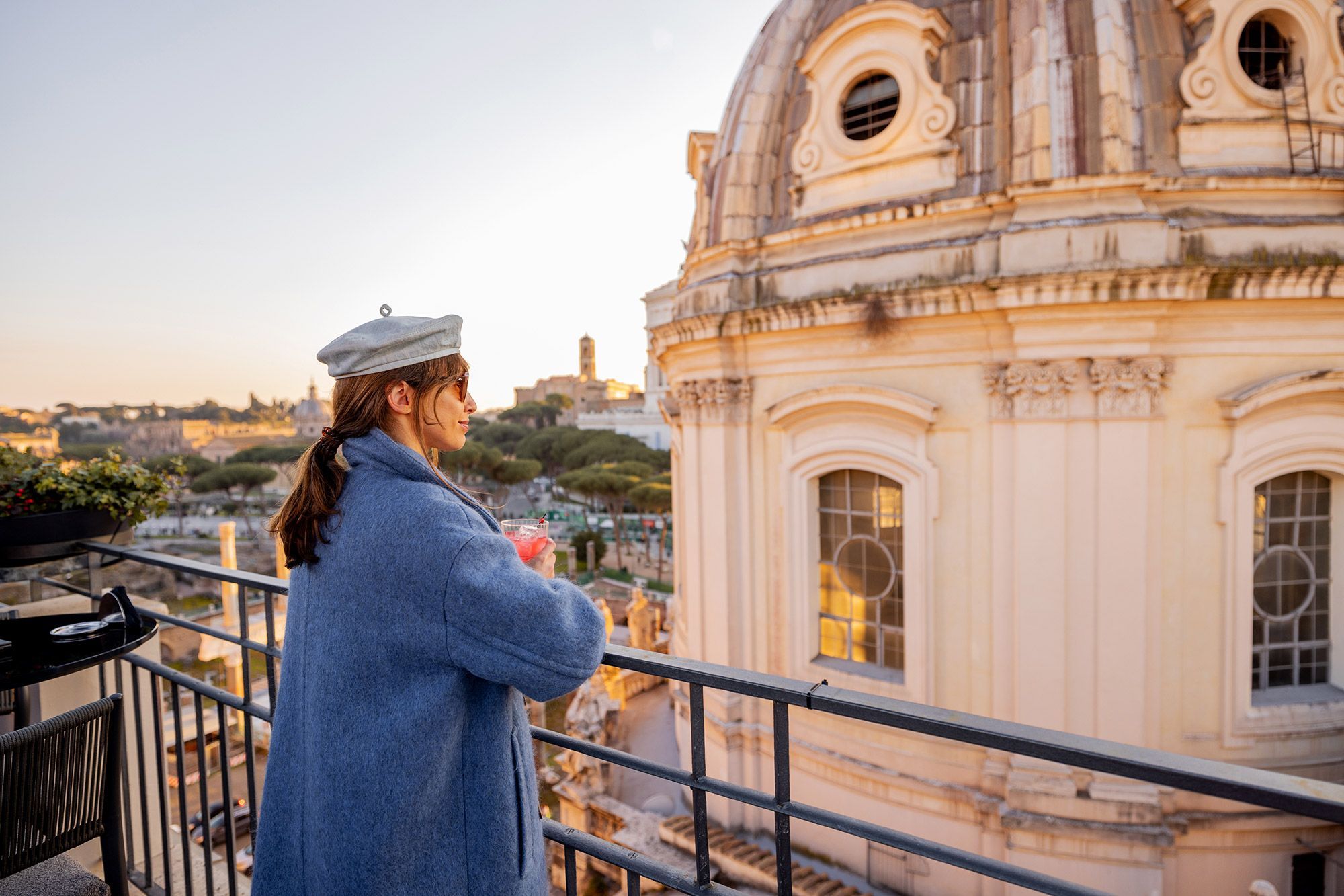 A woman with a drink in her hand standing on a rooftop terrace in Rome, Italy.