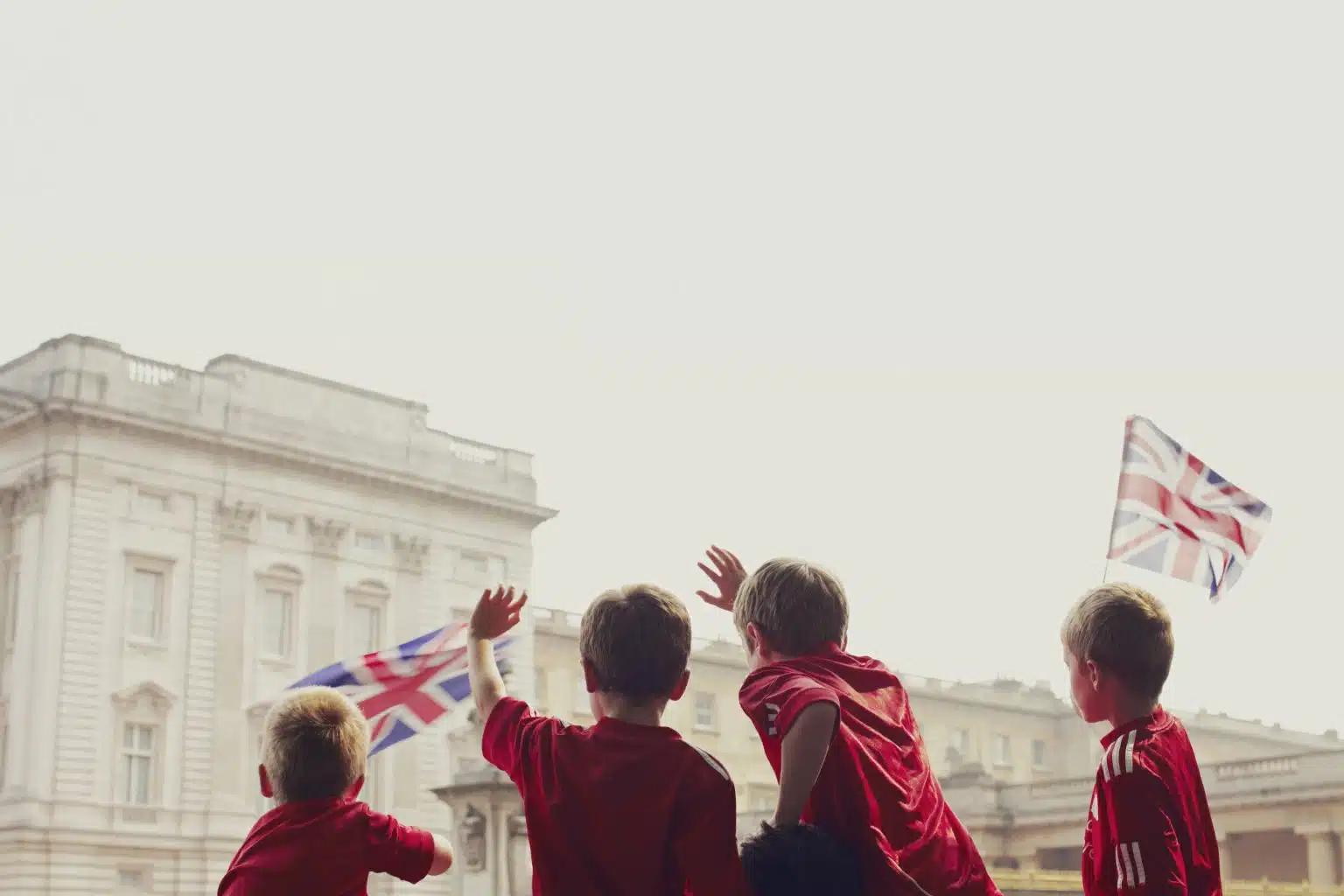 Four children wearing red football t-shirts wave Union Jack flags at Buckingham Palace in London