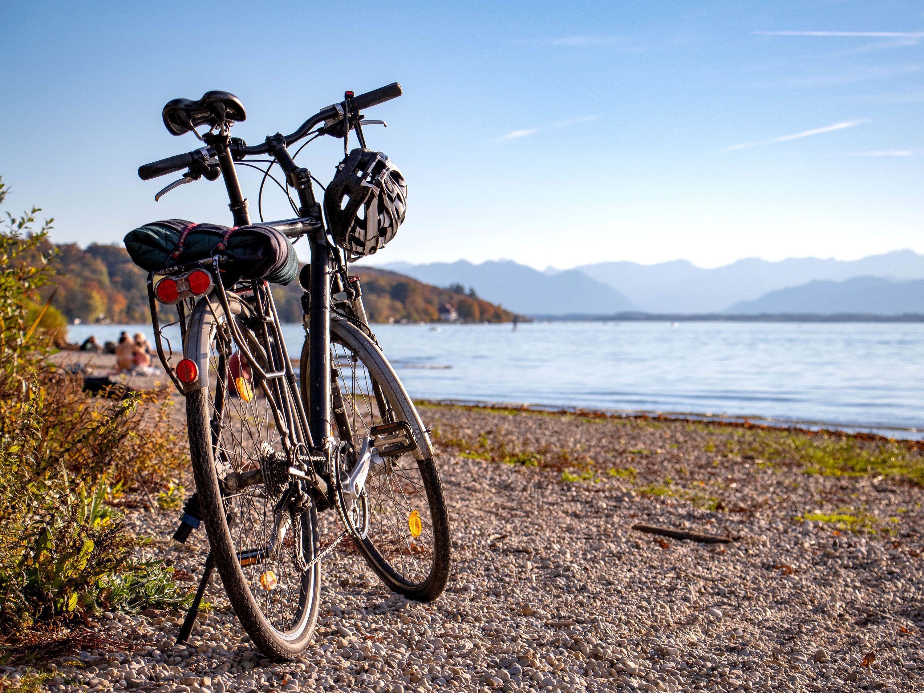 Bicycle and helmet on rocky beach with calm water and mountain in the distance.