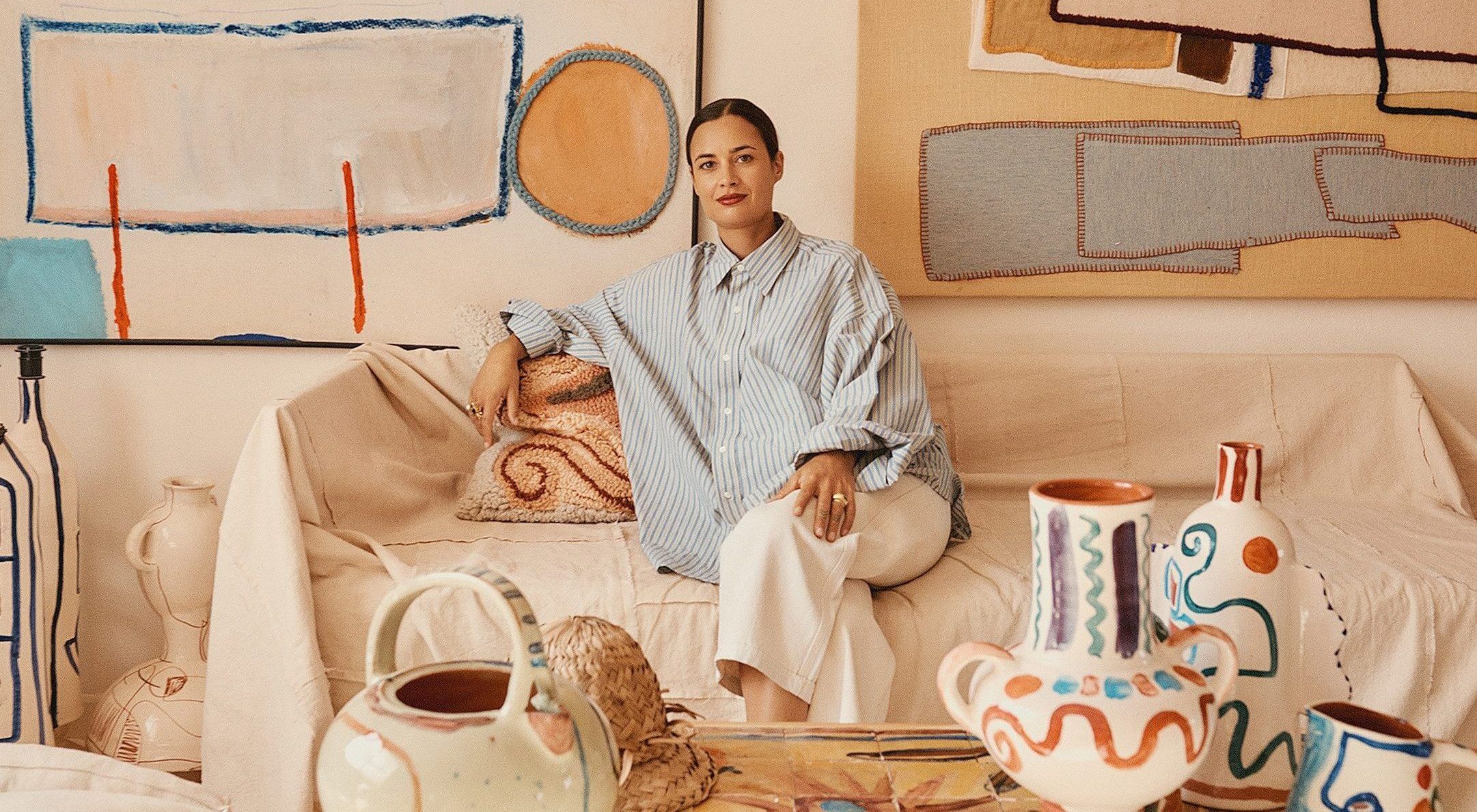 Artist Laurence Leenaert sits on a fabric-draped sofa in her Marrakech studio, surrounded by her hand painted ceramics and paintings