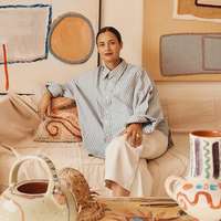 Artist Laurence Leenaert sits on a fabric-draped sofa in her Marrakech studio, surrounded by her hand painted ceramics and paintings