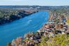 A winding river flows past hillside homes and greenery under a clear blue sky.