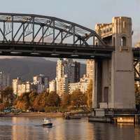 Vancouver's Burrard Street Bridge, which spans False Creek, list in evening sunlight, with a tiny boat passing underneath