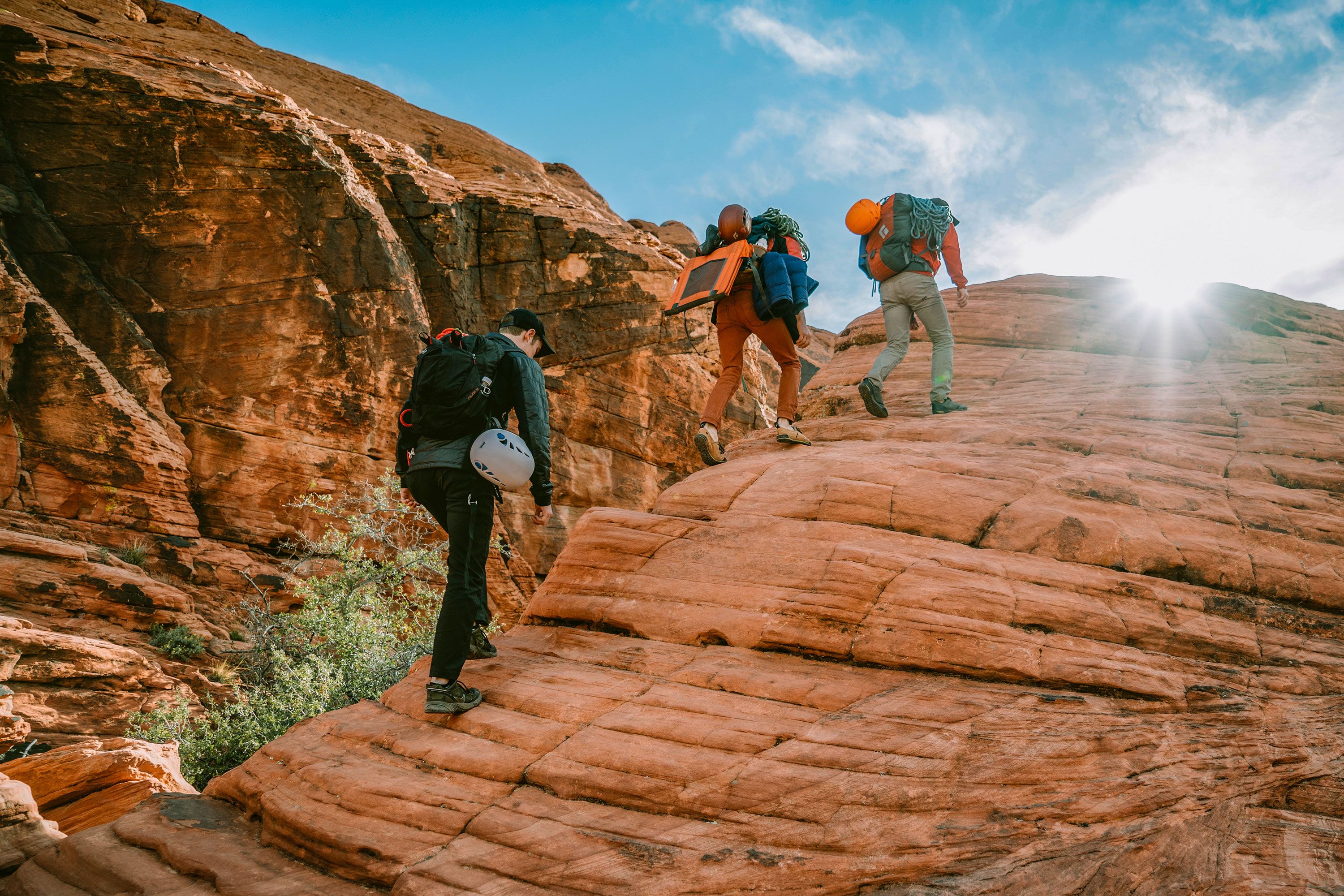 Three hikers climb up step rock with the sun shining down on them.