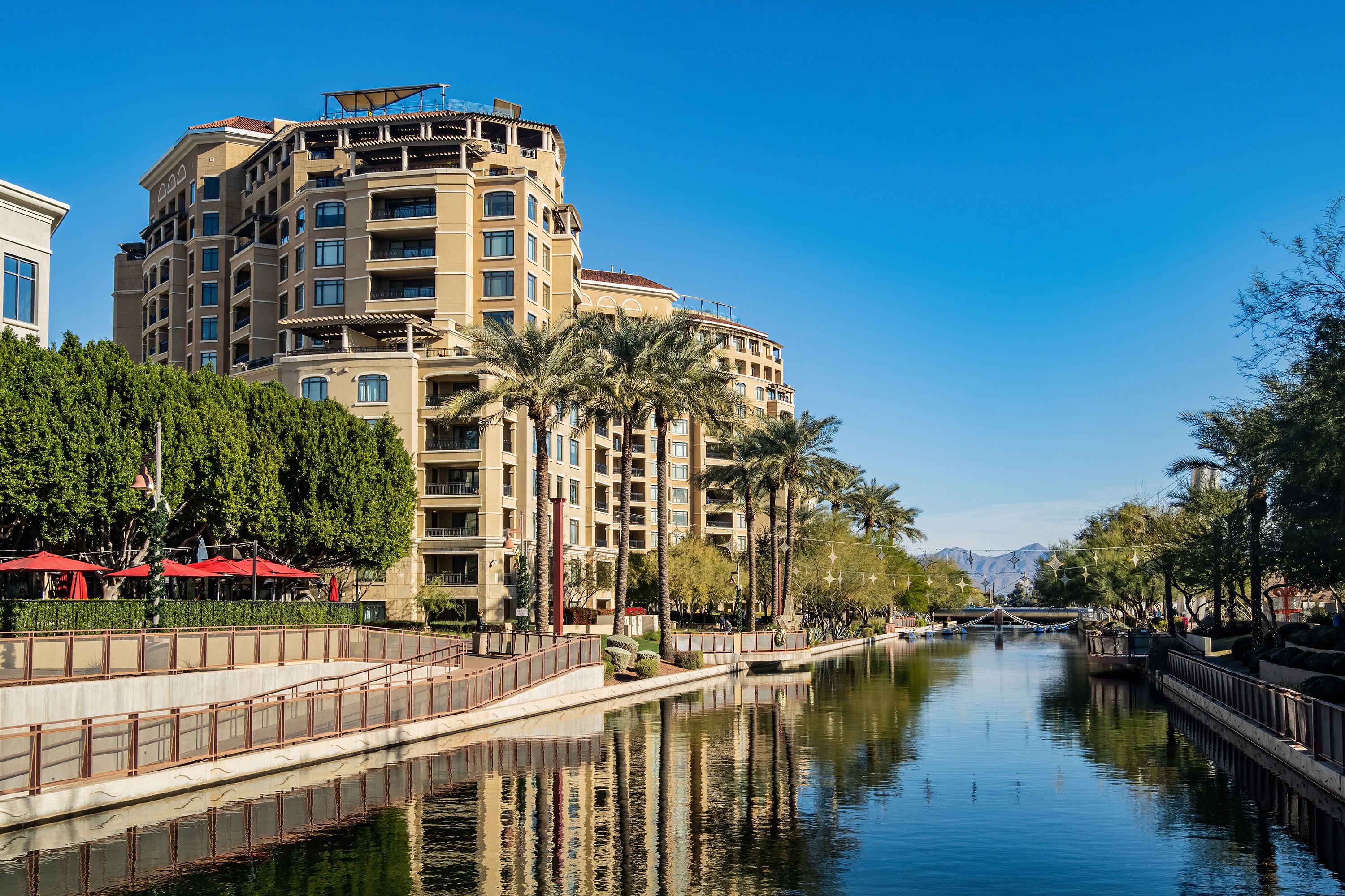 "A canal lined with walkways, trees and buildings on a sunny day with blue skies. Sunny view of the Old Town Scottsdale area"