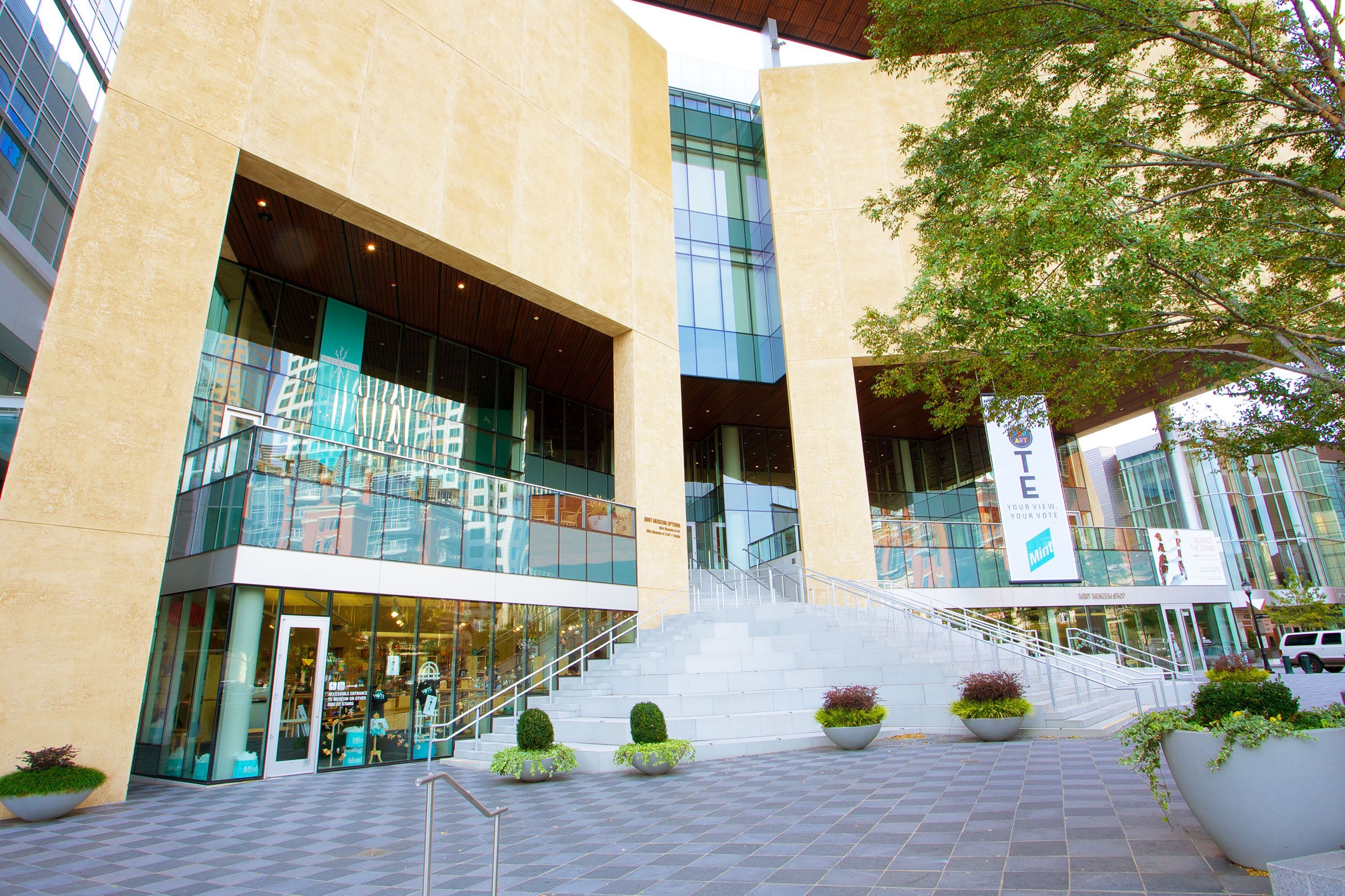 Exterior view of the Mint Museum in Charlotte featuring a sculptural sandstone-colored building with large glass windows.
