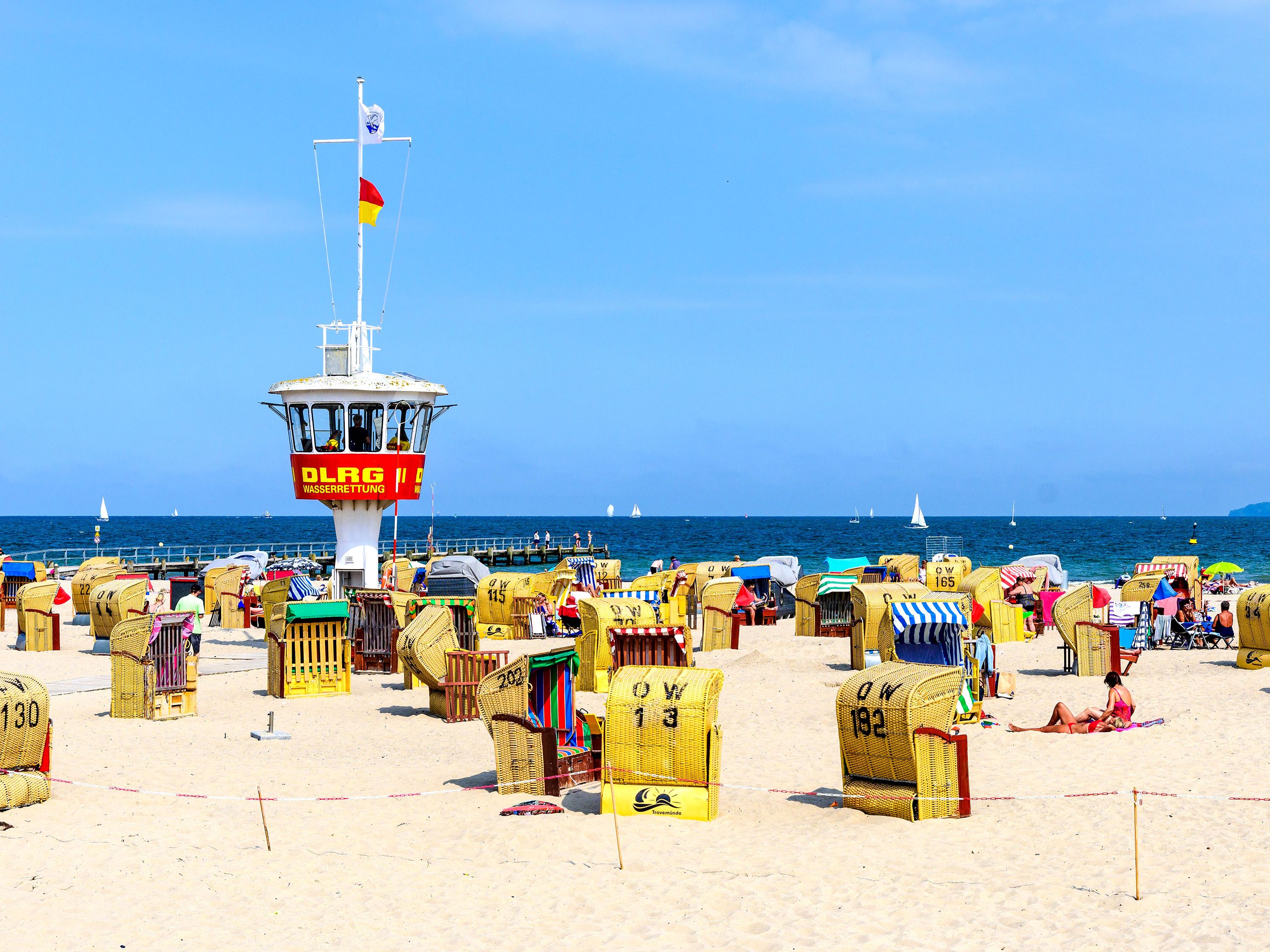 Yellow beach chairs on white sand with blue sky and a red and white lifeguard tower.