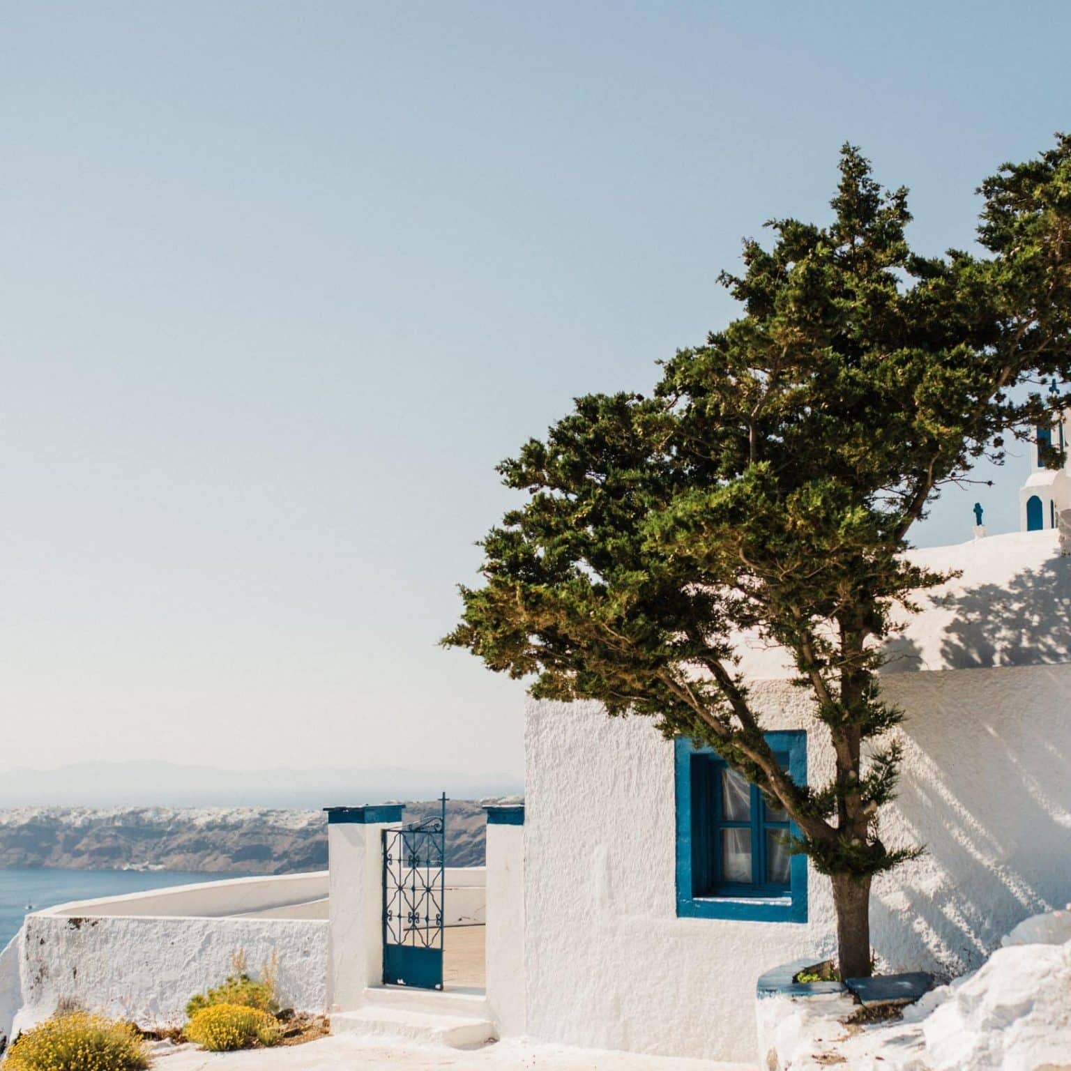 A whitewashed house with bright blue window frames on a hillside in Santorini