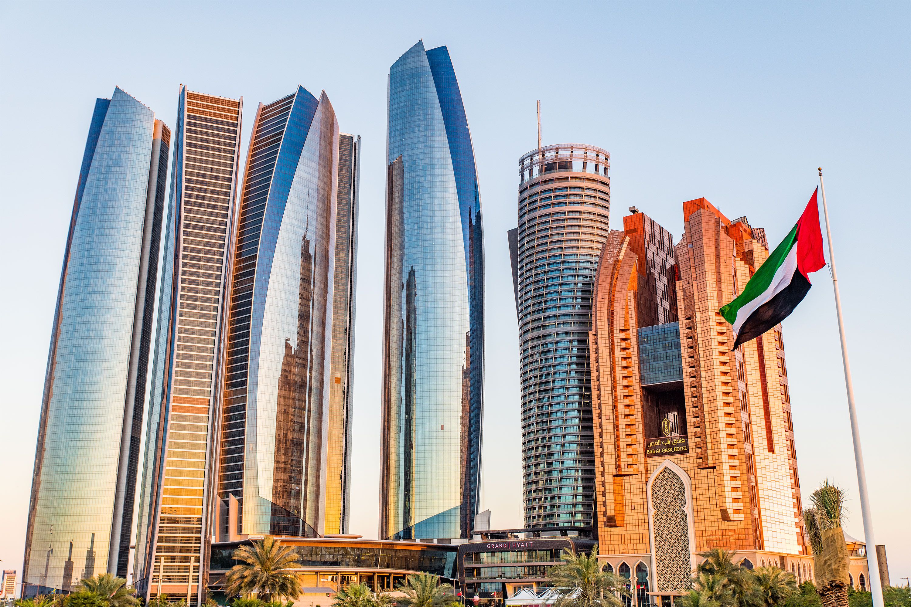 Modern high-rise buildings along a waterfront in Abu Dhabi, with their glass façades reflecting sunlight against a clear sky.