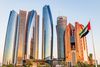 Modern high-rise buildings along a waterfront in Abu Dhabi, with their glass façades reflecting sunlight against a clear sky.