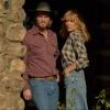 A man and a woman in casual cowboy clothing lean against a wall while looking into the distance