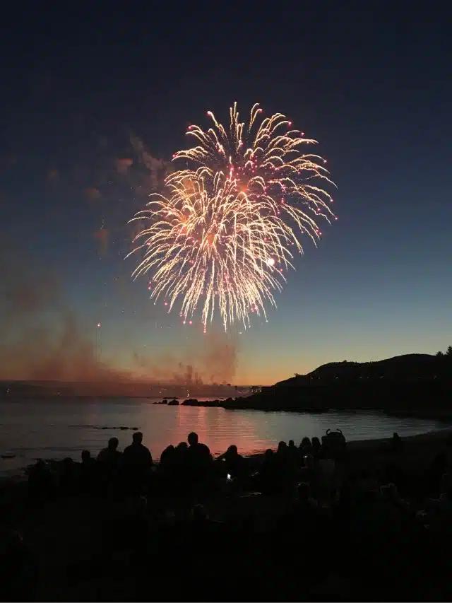 Fireworks blaze over a coastline as a crowd gathers to watch